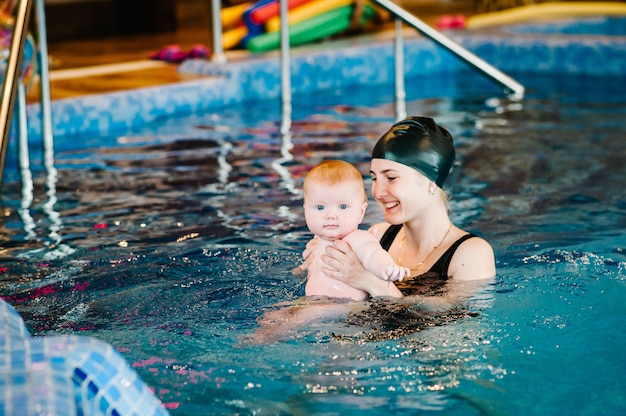 Jovem mãe, instrutor de natação e menina feliz na piscina infantil