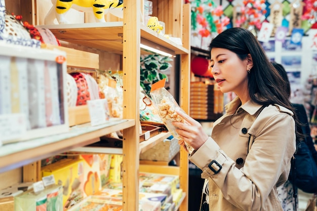 jovem mãe japonesa escolhendo lanche para crianças na loja de especialidades locais em dotonbori osaka japão. mãe asiática comprando biscoitos de comida para a família depois do trabalho no fornecedor. bela dama lendo a marca.