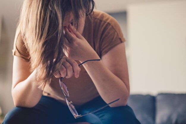 Jovem mãe milenar em casa com óculos graduados de cabeça para baixo triste e deprimida