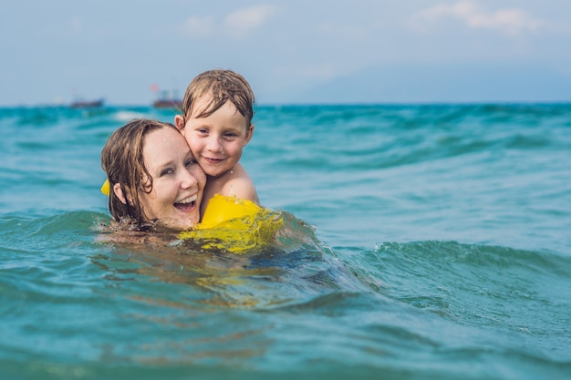 Jovem mãe nadando e brincando com uma criança do sexo masculino nas águas do mar ou oceano