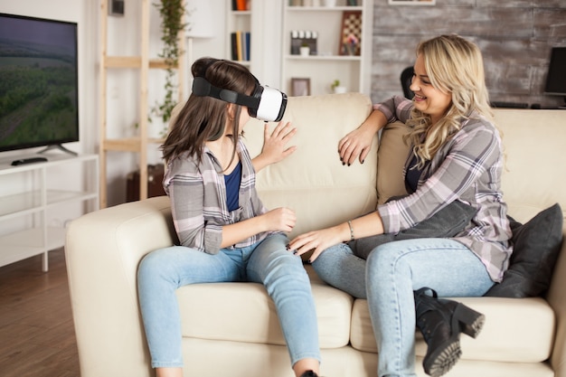 Jovem mãe olhando para sua filha se divertindo com fone de ouvido de realidade virtual. Maternidade moderna.