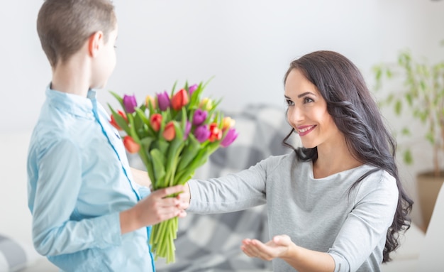 Jovem mãe recebendo um buquê de tulipas de seu filho durante o dia nacional das mães.