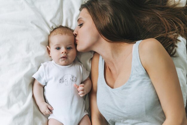 Jovem mãe se divertindo com uma linda garotinha na cama tons naturais amam emoção