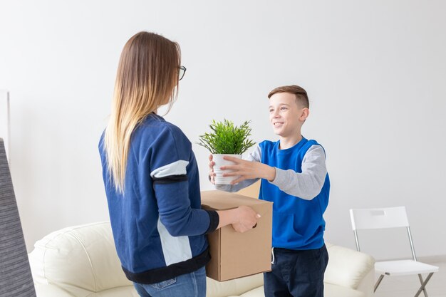 Jovem mãe solteira e um filho brincalhão segurando uma caixa com coisas e uma flor em um vaso na sala de estar de um apartamento novo. Festa de inauguração e novo conceito de habitação.