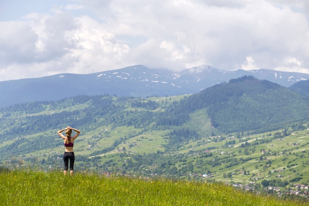 Jovem magro com braços erguidos ao ar livre em fundo de paisagem de montanha bonita num dia ensolarado de verão.