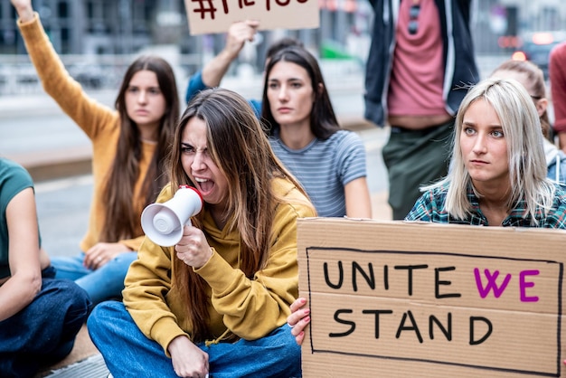 Jovem manifestante feminina dando um slogan usando megafone com grupo de pessoas em segundo plano mulheres protestando por seu empoderamento e futuro