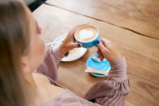 Jovem, mantendo a xícara de café, sentado na mesa de madeira.