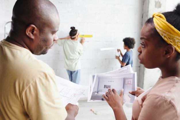 Foto jovem marido e mulher em trajes casuais discutindo papéis com o rascunho e o interior da sala de estar enquanto o filho e a filha os ajudam