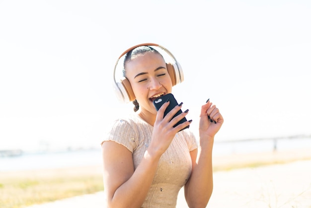 Jovem marroquina ao ar livre ouvindo música com um celular e cantando
