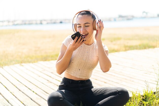 Jovem marroquina ao ar livre ouvindo música com um celular e cantando