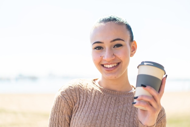 Jovem marroquina ao ar livre segurando um café para viagem com expressão feliz