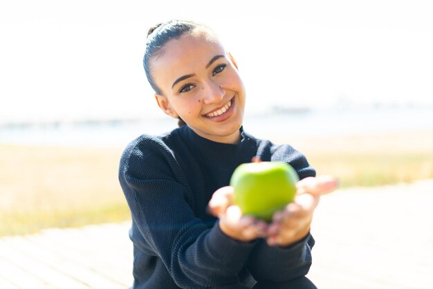 Foto jovem marroquina ao ar livre segurando uma maçã com expressão feliz