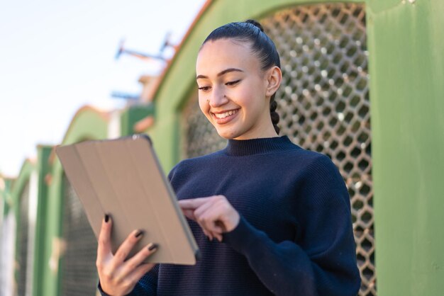 Foto jovem marroquina ao ar livre tocando a tela do tablet com expressão feliz