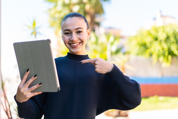 Jovem marroquina segurando um tablet ao ar livre e apontando-o