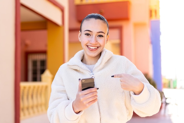 Jovem marroquina usando telefone celular ao ar livre com expressão facial de surpresa