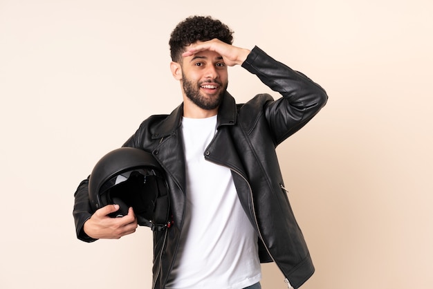 Jovem marroquino com um capacete de motociclista isolado em um fundo bege fazendo gesto surpresa enquanto olha para o lado