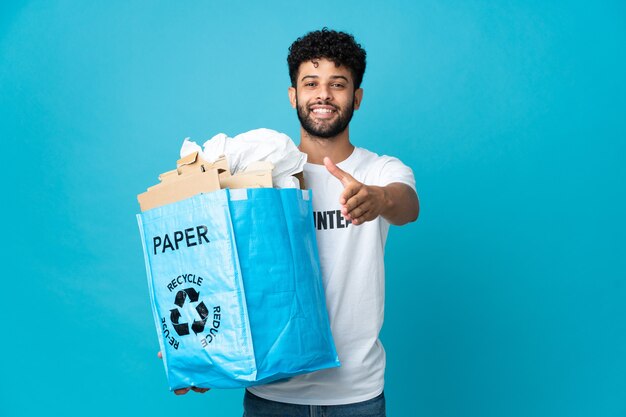 Jovem marroquino segurando uma sacola cheia de papel para reciclar sobre uma parede isolada apertando as mãos para fechar um bom negócio