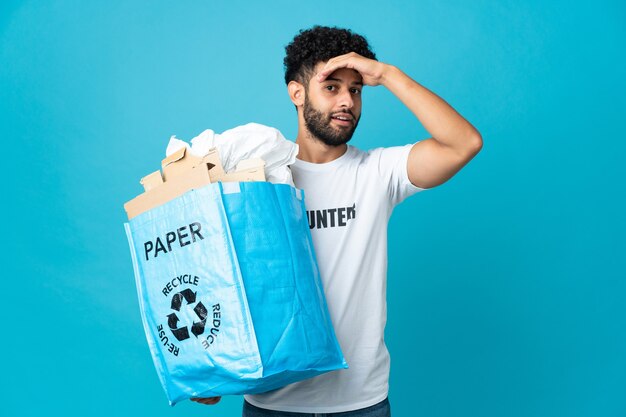 Jovem marroquino segurando uma sacola de reciclagem cheia de papel para reciclar fazendo gesto surpresa enquanto olha para o lado