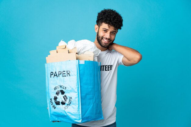 Jovem marroquino segurando uma sacola de reciclagem cheia de papel para reciclar sobre uma parede isolada rindo