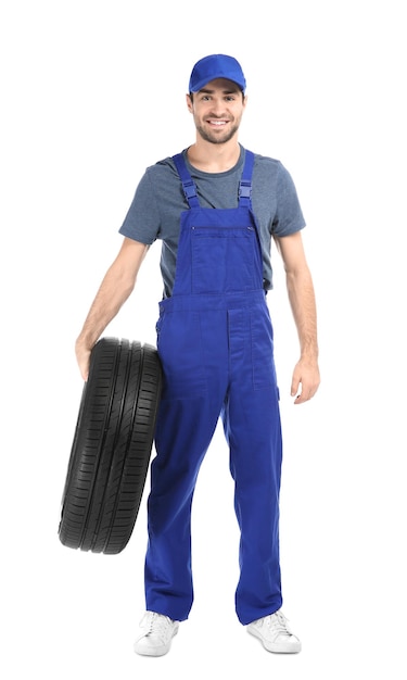 Jovem mecânico de uniforme com pneu de carro em fundo branco