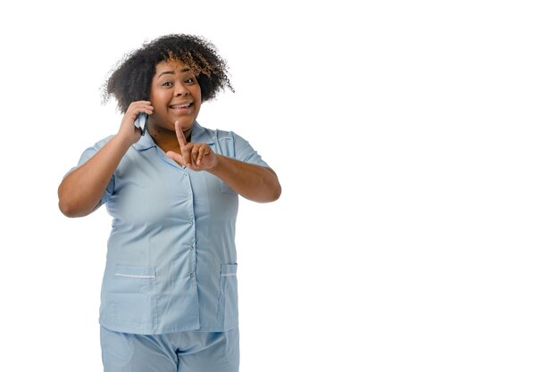 Jovem médica afrolatina sorrindo falando ao telefone com um dedo levantado fundo branco
