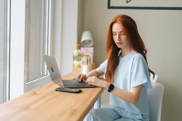 Jovem médica alegre usando uniforme médico verde azul, digitando no laptop