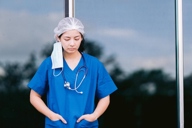 Jovem médica de fato de proteção, uniforme e máscara de rosto, exausta e preocupada.