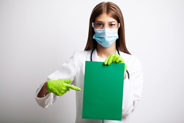 Jovem médica em uma máscara detém uma folha de papel em branco