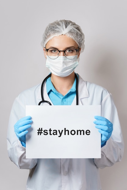 Jovem médica está segurando um papel com a hashtag #stayhome