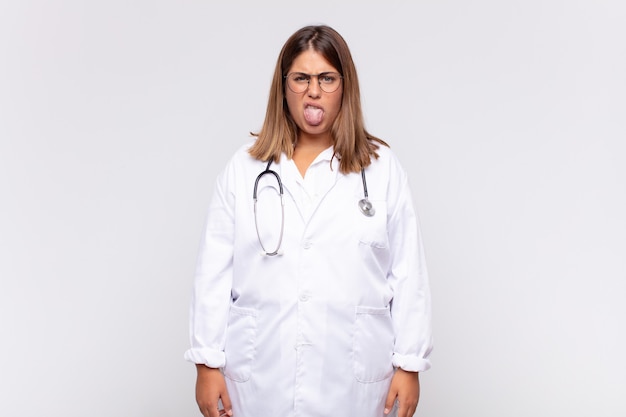 Jovem médica sentindo-se enojada e irritada, mostrando a língua, não gostando de algo nojento e nojento