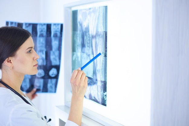 Foto jovem médica sorridente com estetoscópio apontando para raio x no consultório médico