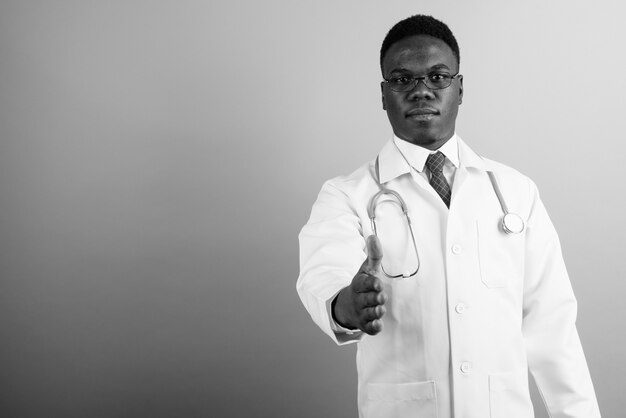 jovem médico africano usando óculos contra uma parede branca. Preto e branco