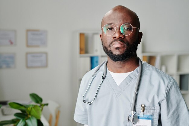 Jovem médico afro-americano contemporâneo em pé no consultório médico
