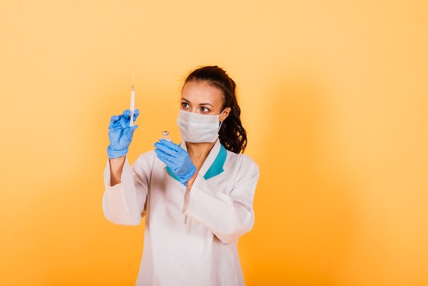 Jovem médico afro-americano sorridente com máscara médica segurando uma seringa