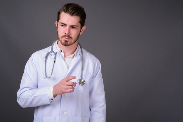 Jovem médico barbudo bonito contra uma parede cinza