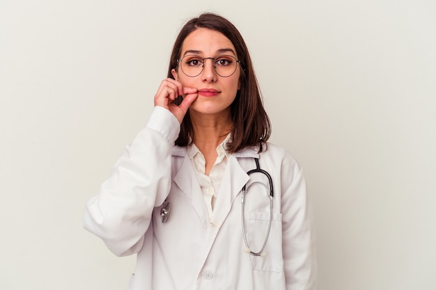 Jovem médico caucasiana, isolada no fundo branco com os dedos nos lábios, mantendo um segredo.