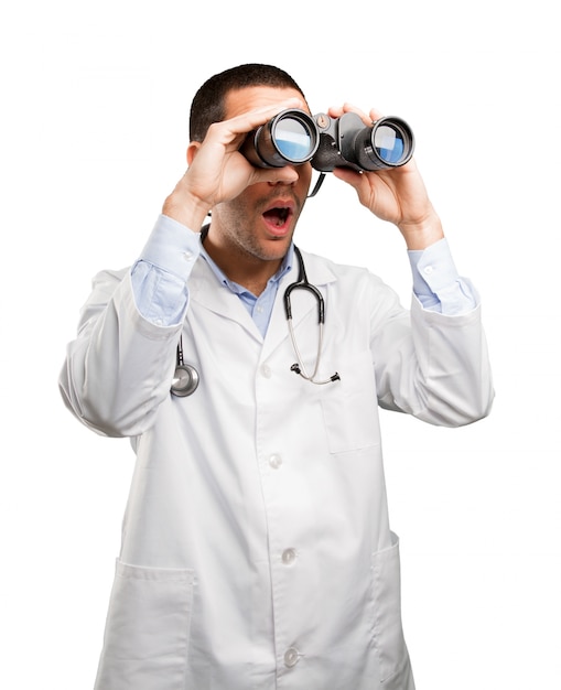 Foto jovem médico chocado usando um binóculo
