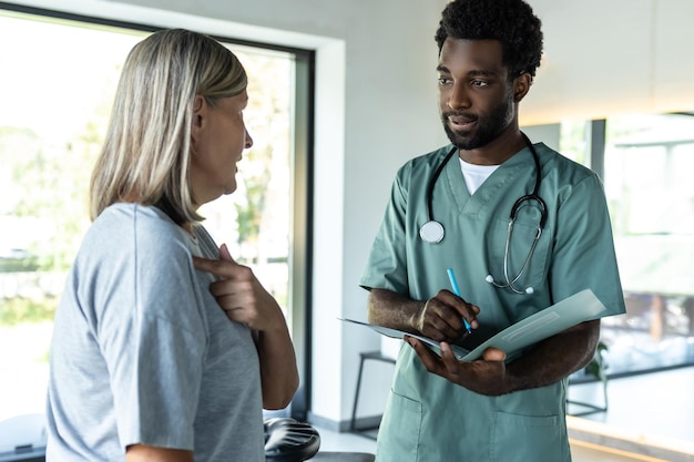 Jovem médico de pele escura falando com uma paciente em uma clínica de reabilitação