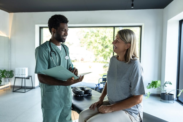 Jovem médico de pele escura falando com uma paciente em uma clínica de reabilitação