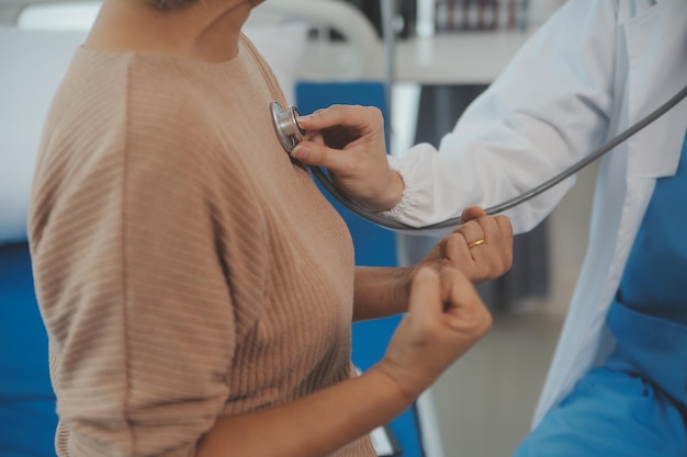 Jovem médico está usando um estetoscópio ouvir o batimento cardíaco do paciente Foto de uma médica dando um paciente masculino um check-up