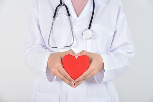 Jovem médico feminino com estetoscópio segurando coração vermelho nas mãos em branco