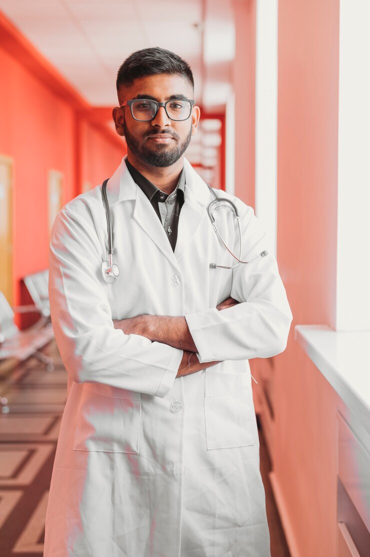 Jovem médico indiano sorridente usando óculos e um estetoscópio em uma vista frontal de jaleco branco