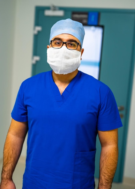 Foto jovem médico irreconhecível com máscara facial branca, chapéu médico e bata azul retrato de médico profissional closeup