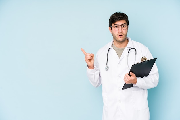 Jovem médico isolado em azul apontando para o lado