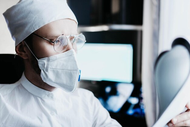 jovem médico masculino de uniforme branco e óculos no escritório funciona