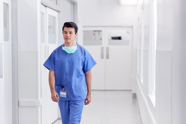 Jovem médico masculino vestindo aventais caminhando ao longo do corredor do hospital