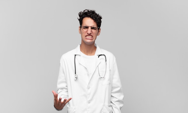 Jovem médico parecendo zangado, irritado e frustrado gritando wtf