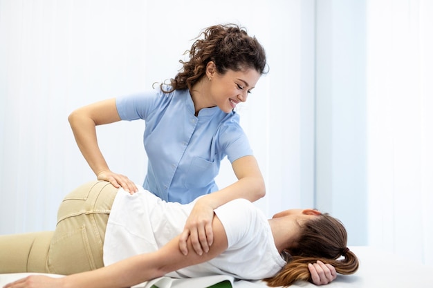 Jovem médico quiroprático ou osteopata consertando mulher deitada de costas com movimentos de mãos durante a visita na clínica de terapia manual quiroprático profissional durante o trabalho