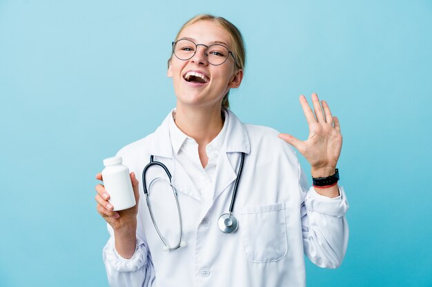 Jovem médico russo segurando o frasco de comprimidos em azul, mostrando o número dez com as mãos