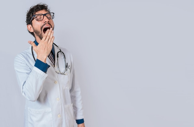 Jovem médico sonolento bocejando em fundo isolado Cansado do conceito médico de trabalho Médico cansado e sonolento isolado